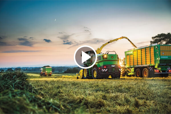 Tractors and trailers harvesting grass at dusk